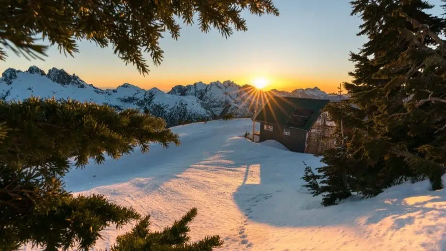 A custom designed cabin sits atop a mountain with a sunset backdrop