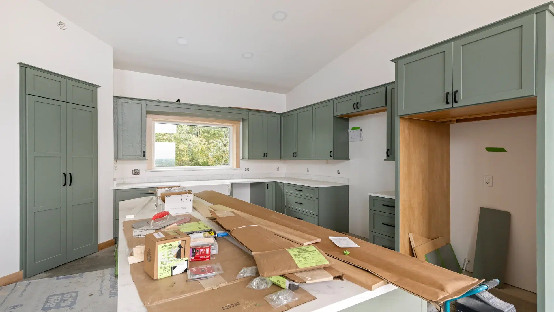 Green painted kitchen cabinetry fits among the forest backdrop