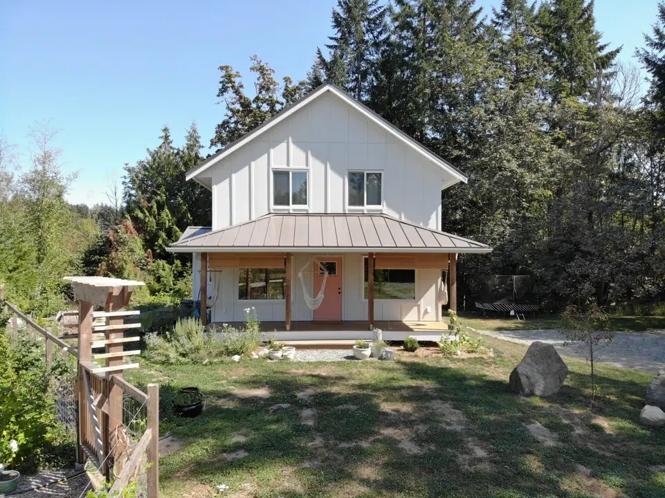 A small, two story cottage surrounded by gardens